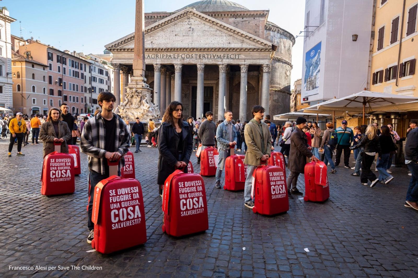 Persone in piedi al Pantheon con valigie rosse per campagna Cosa Salveresti