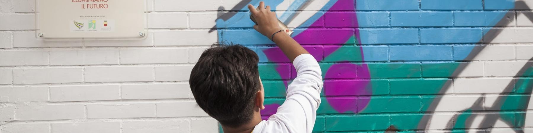 bambino al di fuori di un punto luce di save the children italia disegna un murales