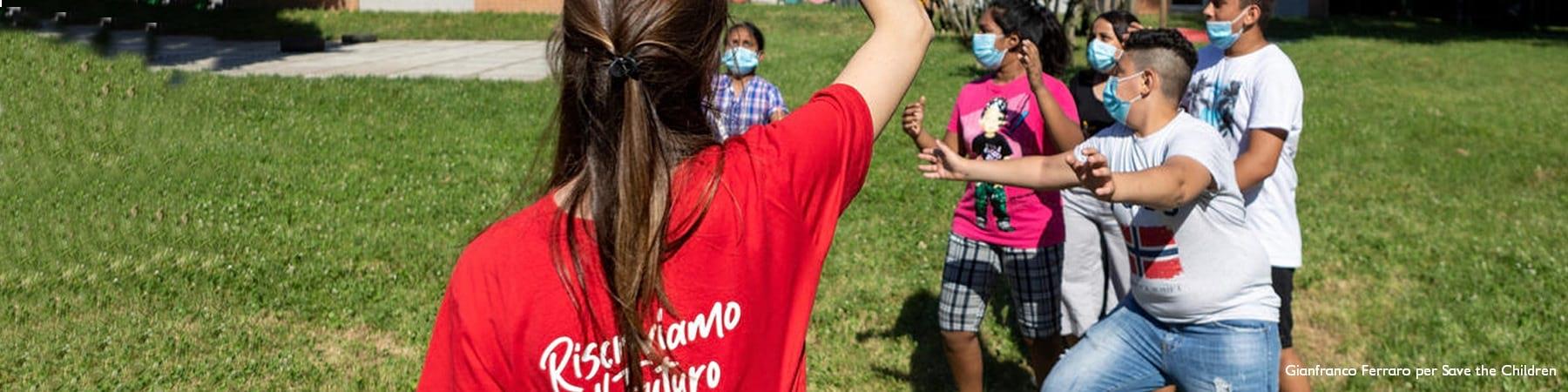 Un'operatrice Save the Children gioca in un prato con alcuni bambini 