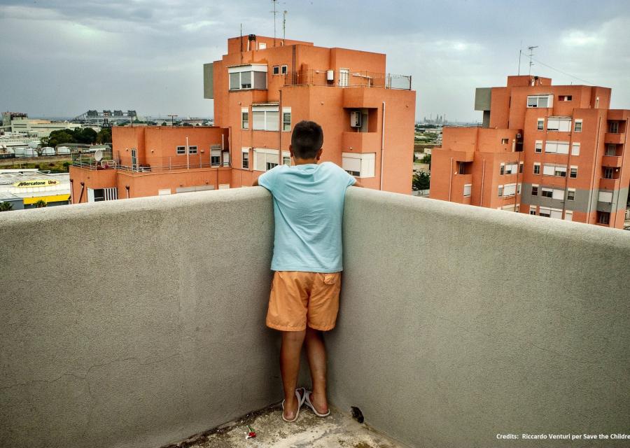 bambino su un balcone di spalle in piedi guarda gli edifici arancioni davanti a sè