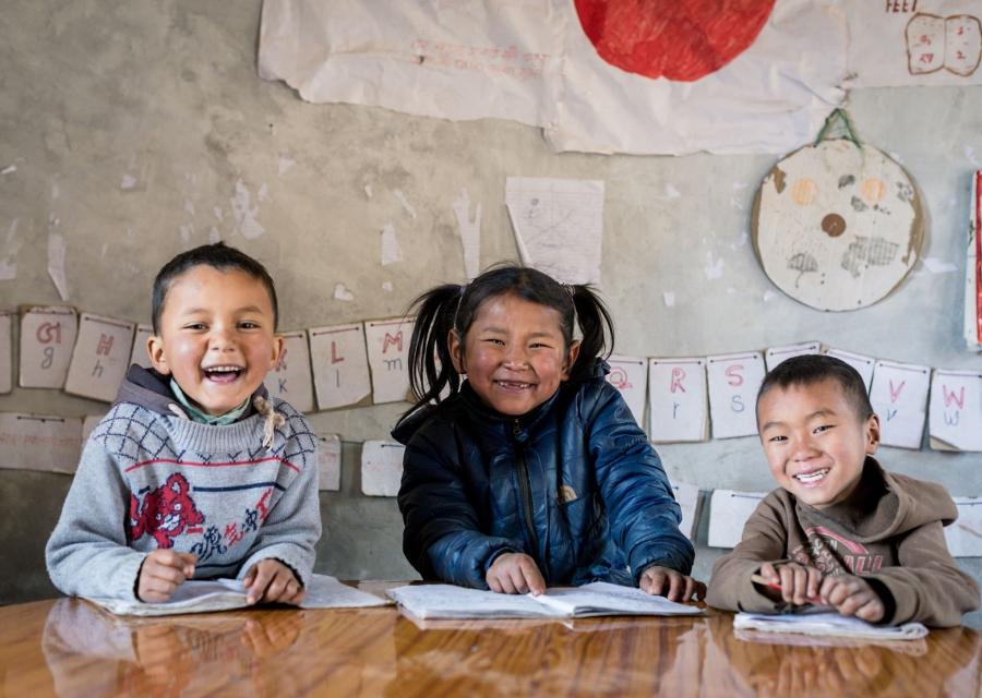 Tre piccoli studenti nepalesi sorridono e guardano in camera mentre si godono la scuola, con quaderni e penne