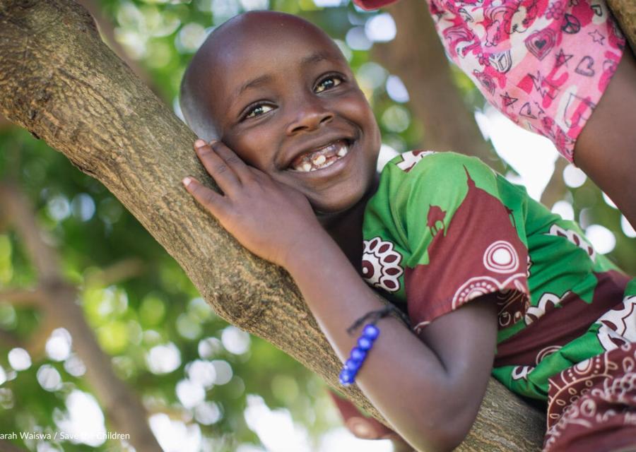 bambina sorridente appoggiata a ramo di albero 