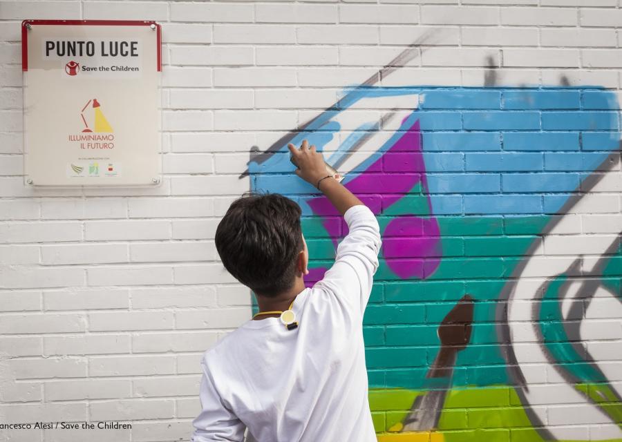 bambino al di fuori di un punto luce di save the children italia disegna un murales