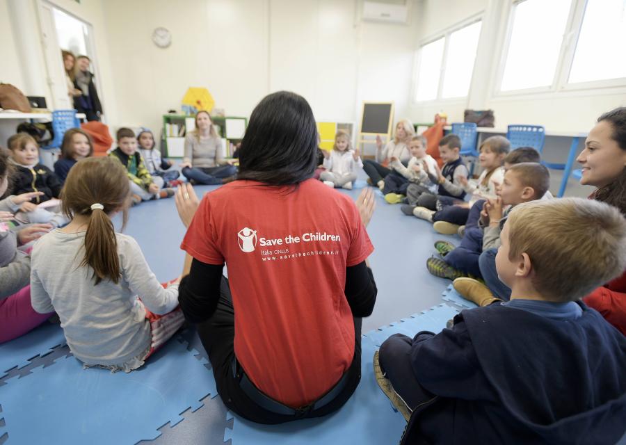 operatrice save the children Italia di spalle in cerchio con dei bambini durante un attività in post emergenza