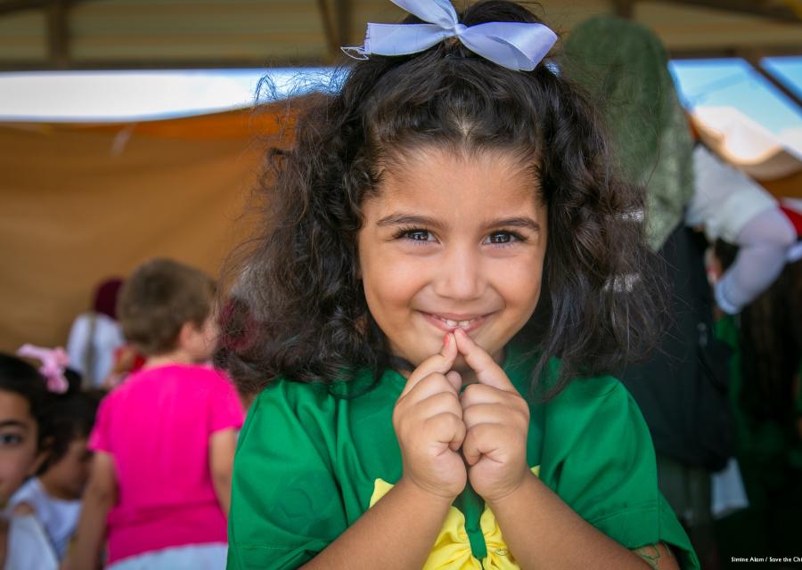 bambina con capelli castani vestita di verda e giallo tiene le mani davanti al viso mentre sorride