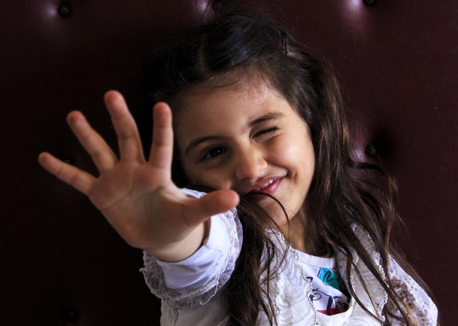 Bambina Siriana primo piano. Fa l'occhiolino e mostra la mano aperta.