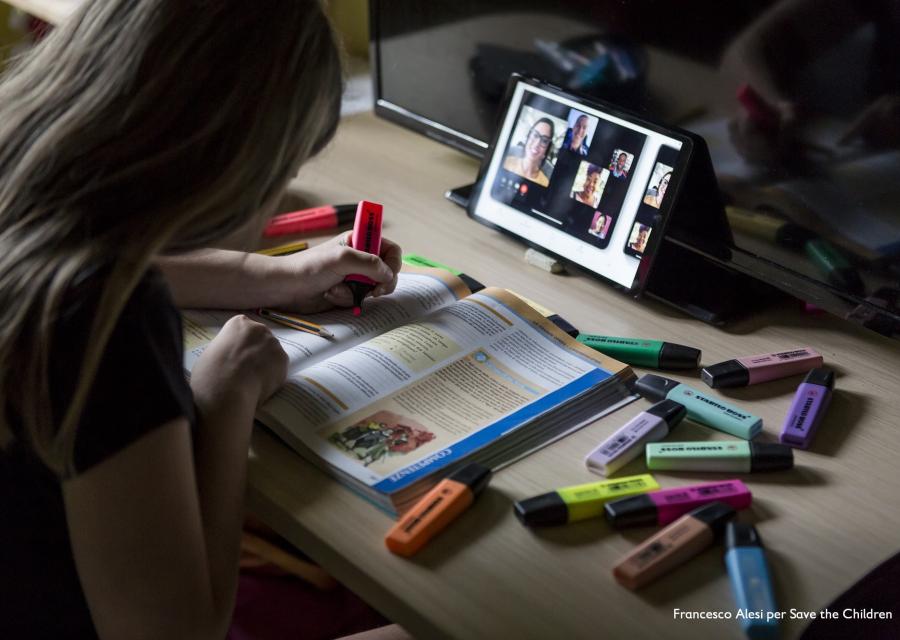 bambina seduta alla scrivania evidenzia un libro di scuola durante una lezione a distanza con tablet
