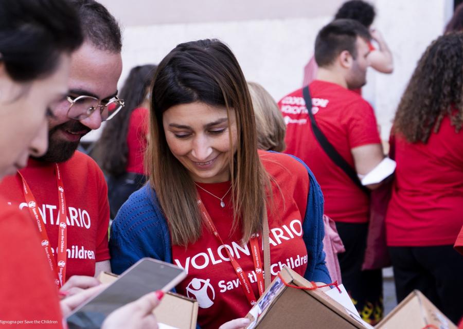 ragazza volontaria save the children insieme altri ragazzi volontari tutti con maglietta rossa dei volontari che leggono una brochure