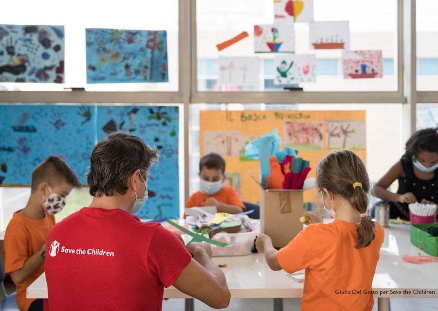 operatore di spalle con maglietta rossa e logo di save the children mentre insegna a quattro bambini nel Punto Luce di Roma