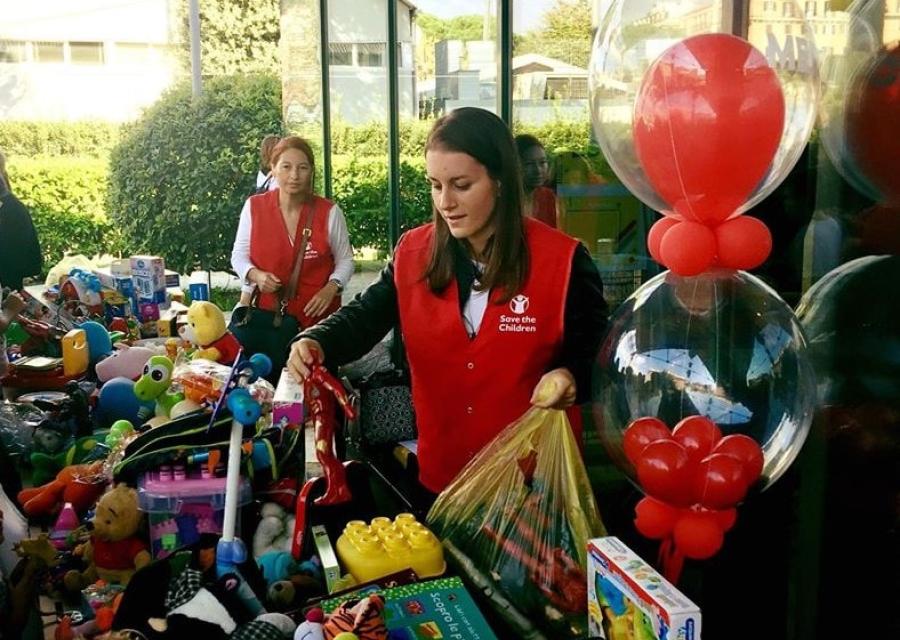 due volontarie di save the children davanti a un banco con tanti giochi per raccogliere fondi per i bambini