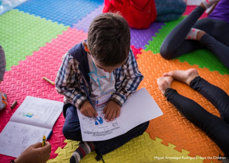 bambino seduto a gambe incrociate su un tappeto colorato intento a leggere