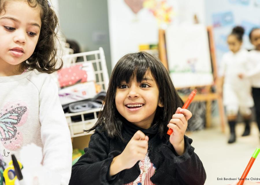 due bambine sorridenti in primo piano una ha in mano un pennarello