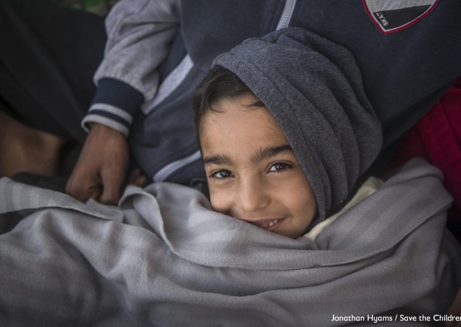 Un bambino con cappuccio grigio in testa sorride avvolto in una coperta anche essa grigia.