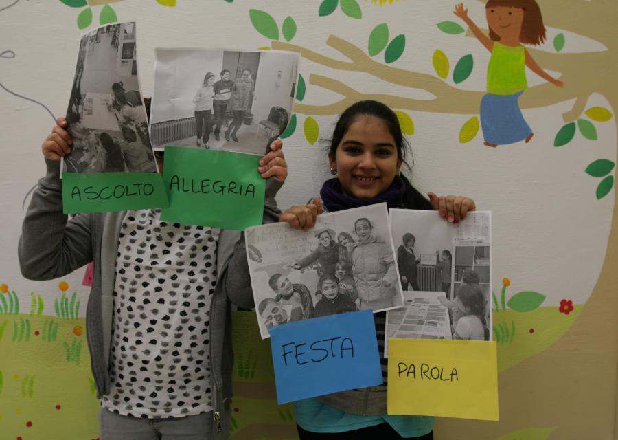 2 ragazze davanti a un muro colorato tengono in mano dei disegni e li mostrano