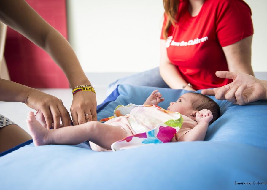 3 operatrici save the children Italia al fianco di un neonato sdraiato su un cuscino blu