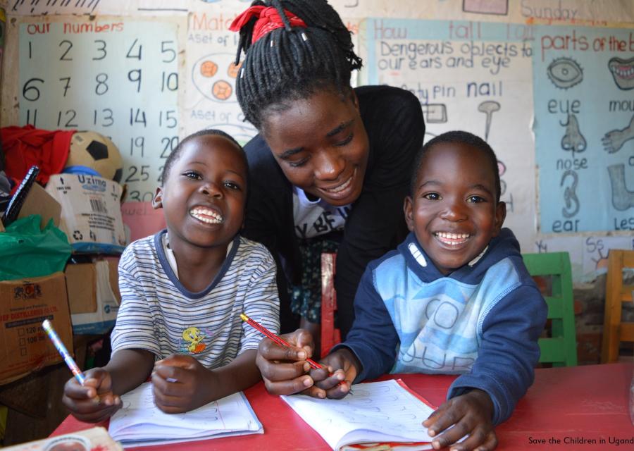 2 bimbi con la maestra studiano sorridenti seduti al banco di scuola