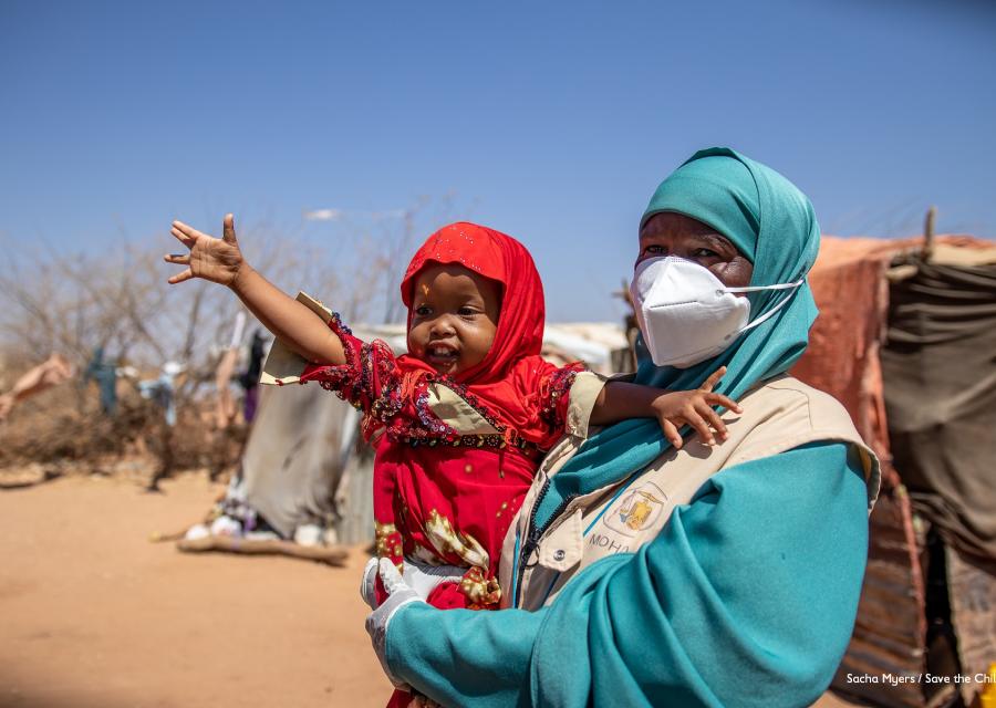 Bambina della Somalia vestita di rosso è in braccio a una operatrice save the children e ha il braccio alzato verso l alto