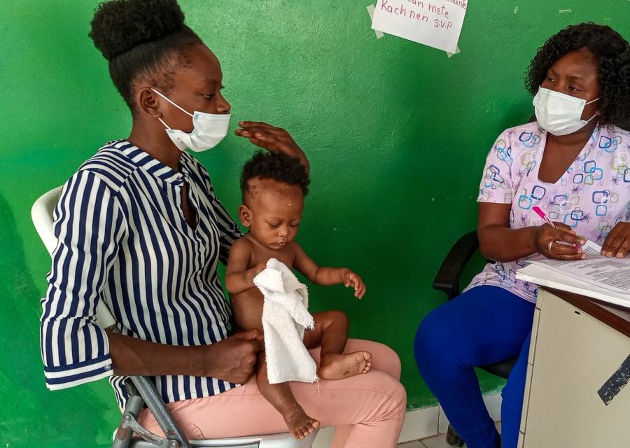 Una donna con in braccio il suo bimbo neonato durante una visita con un infermiera
