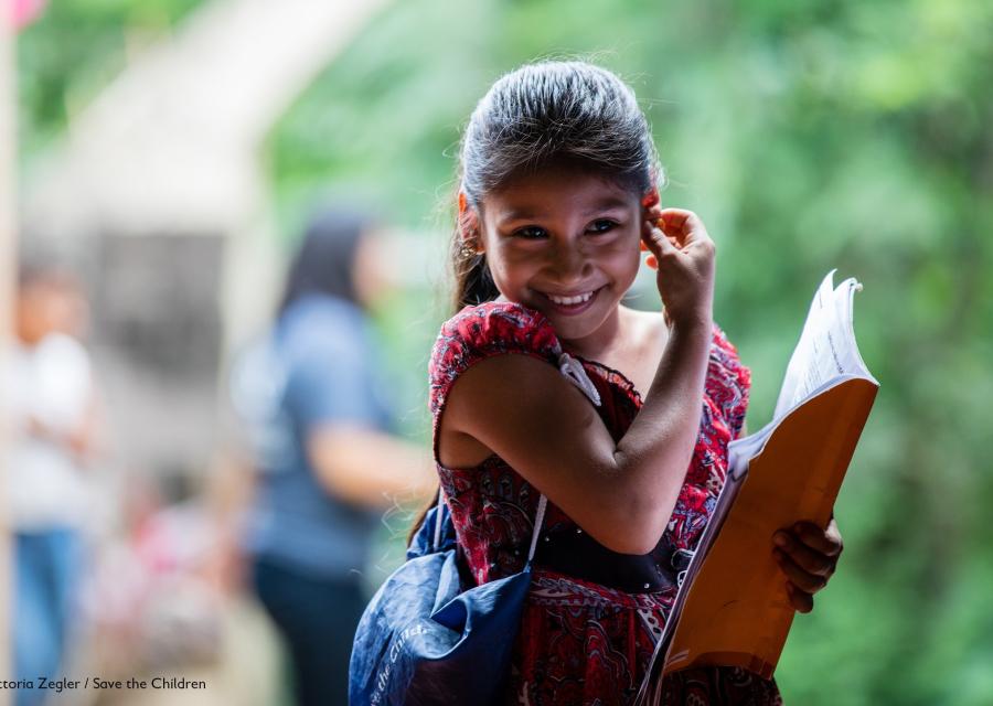 Bambina di El Salvador sorridente con una borsa a tracolla e un libro in mano