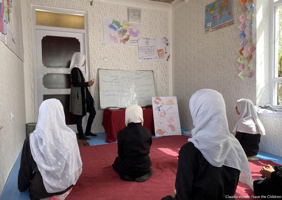 Bambine afghane sedute in ginocchio per terra in una classe con tappeto rosso.