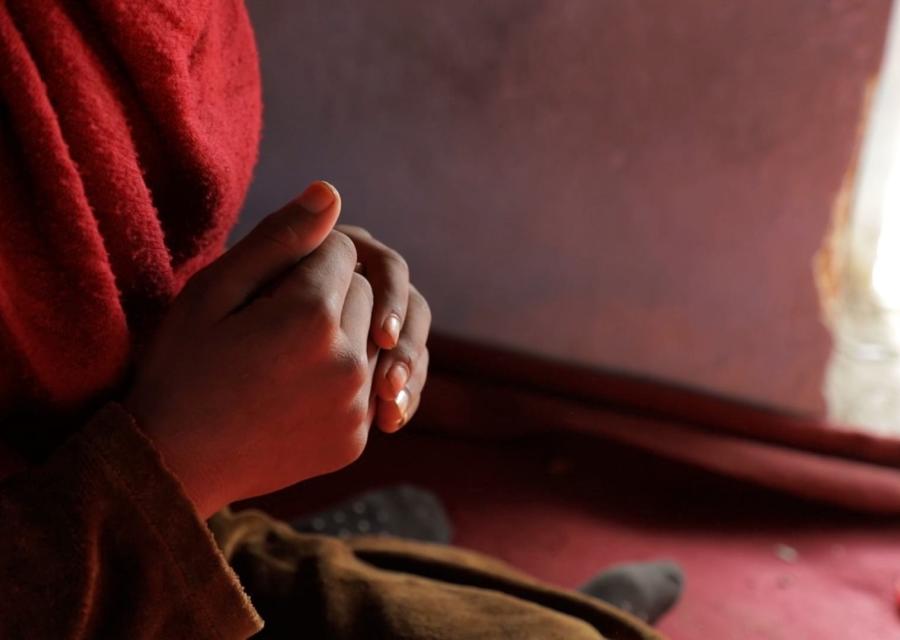 mani giunte di una bambina anonima che indossa un vestito rosso.