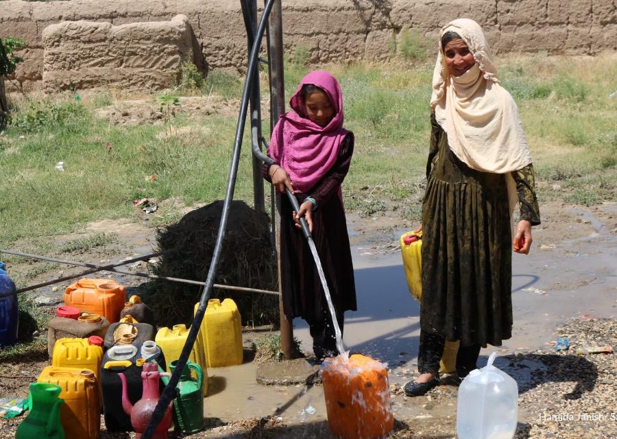Due bambine afghane prendono acqua da una pompa in mezzo a un campo brullo