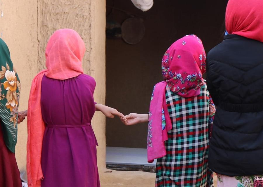 4 bambine afghane di spalle si tengono per mano, indossano chador e vestiti colorati