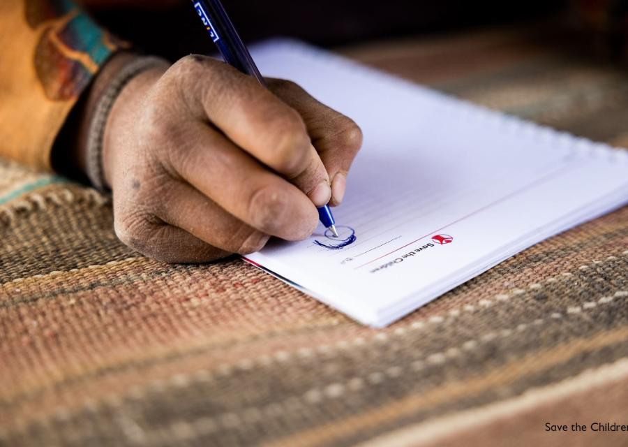 Mano impugna una penna e scrive su carta intestata di save the children