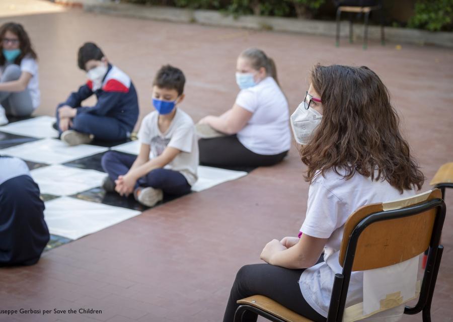 ragazza seduta su una sedia di scuola indossa mascherina e guarda i compagni davanti a lei seduti per terra