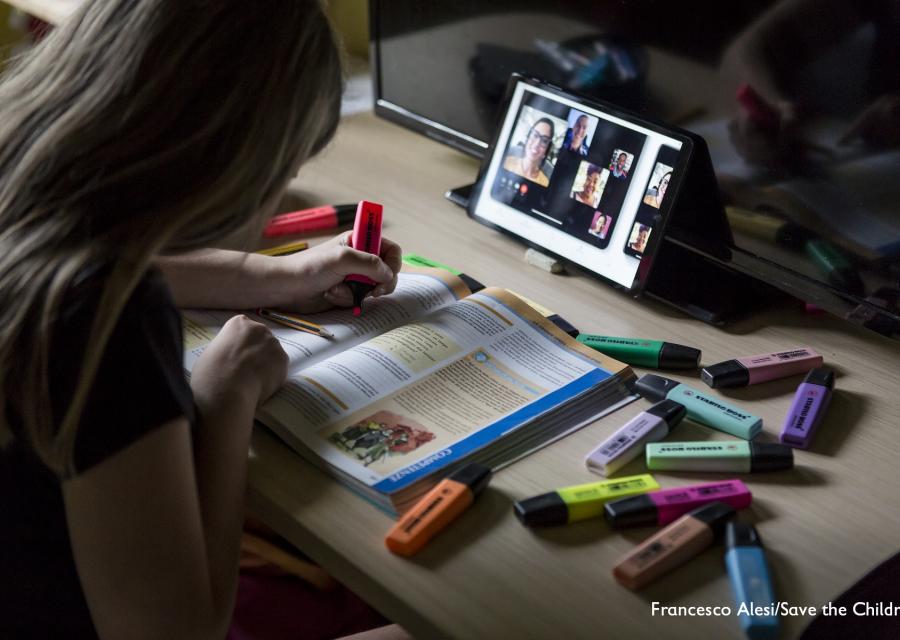 Bambina di spalle evidenzia libro scolastica mentre fa lezione a distanza su un tablet davanti a lei
