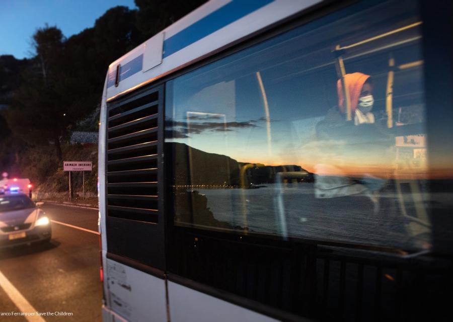 Finestrino di un autobus con riflesso il mare e i colori del tramonto, all'interno di vede un ragazzo seduto 