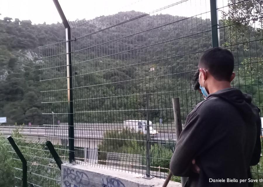 Ragazzo preso di spalle indossa una felpa grigia e guarda davanti a sé. Si trova all aperto e di fronte a sé ha una rete e oltre una collina alberata.