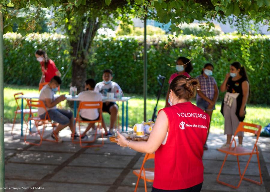 Volontaria in primo piano con un vassoio con sopra la merenda per i ragazzi sullo sfondo del centro Arcipelago educativo 