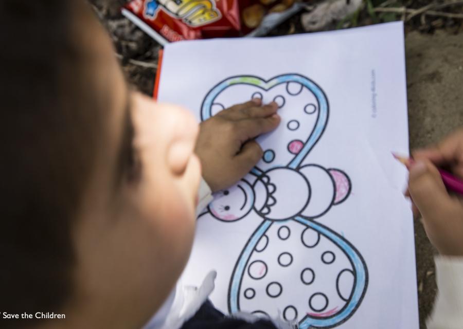 bimbo in primo piano a sinistra sfocato mentre disegna una farfalla colorata su un foglio davanti a sè