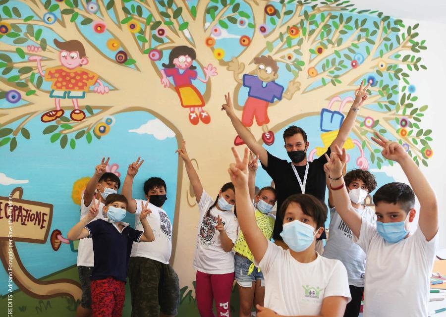 bambini con mani alzate di fronte un murales con albero 