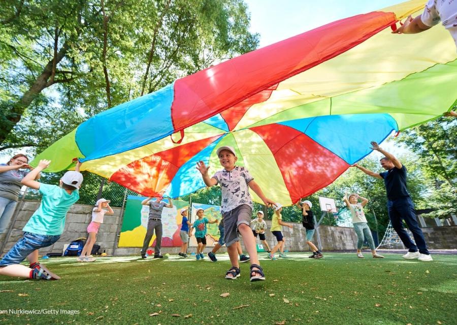 bambini che giocano sorridenti sotto un telo con i colori dell'arcobaleno  