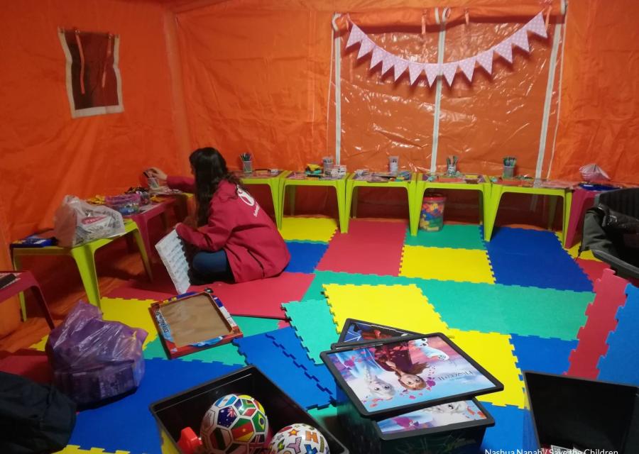 Interno di uno spazio a misura di bambino Save the Children in Romania dove un operatrice sta mettendo a posto i giochi seduta a terra.