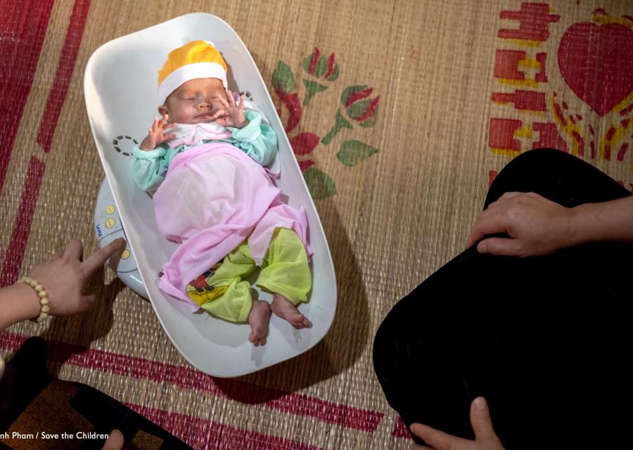 neonato in una vaschetta di plastica per pesarlo, vestito con vestitini caldi e colorati