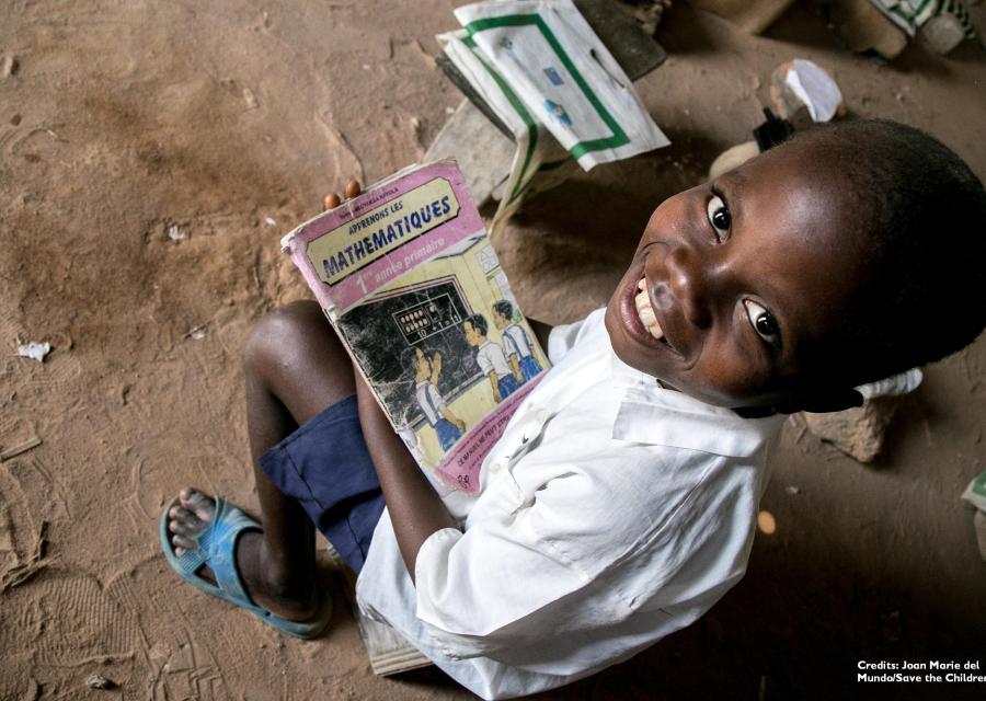 Bambino Repubblica Democratica del Congo foto dall'alto è seudto e guarda in camera tenendo dei libri di scuola in mano.