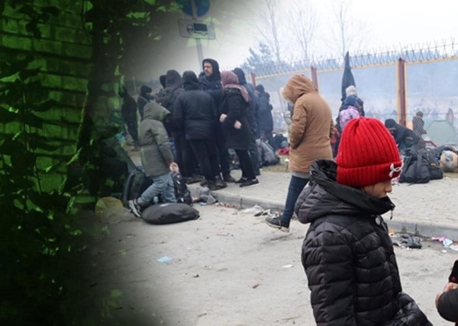 due bambini seduti su un tubo, vestiti invernali. Sullo sfondo altre persone. Sono tutti migranti bloccati al confine con l'Europa. A sinistra della foto una finestra con lue verde simbolo di speranza.