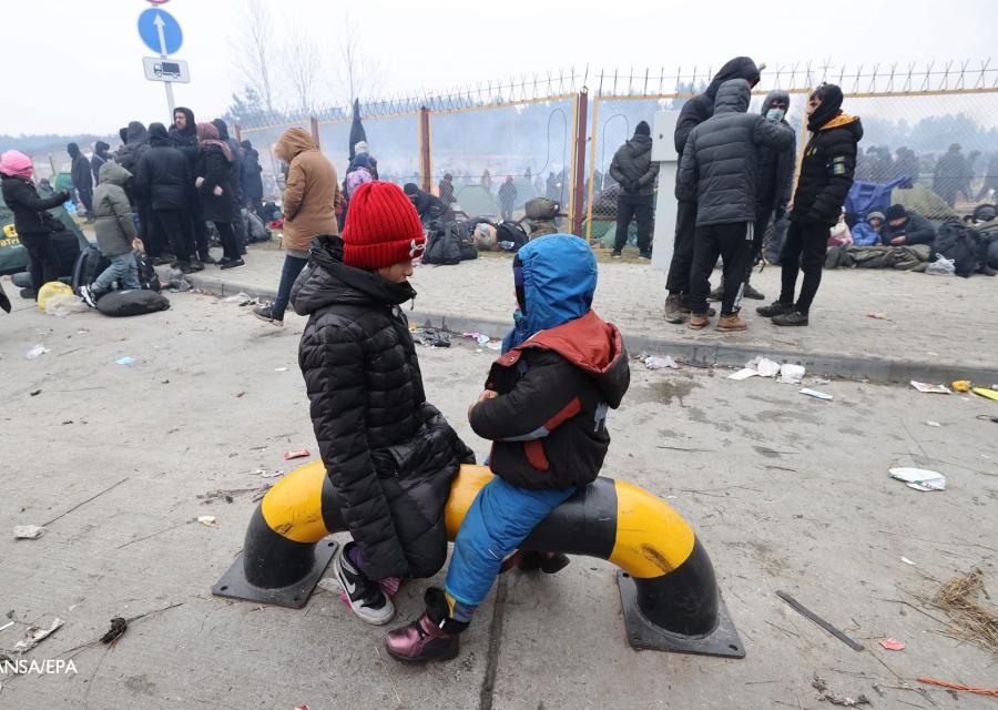 due bambini seduti in strada uno davanti all altro sono presi di profilo e dietro di loro ci sono molti adulti in piedi
