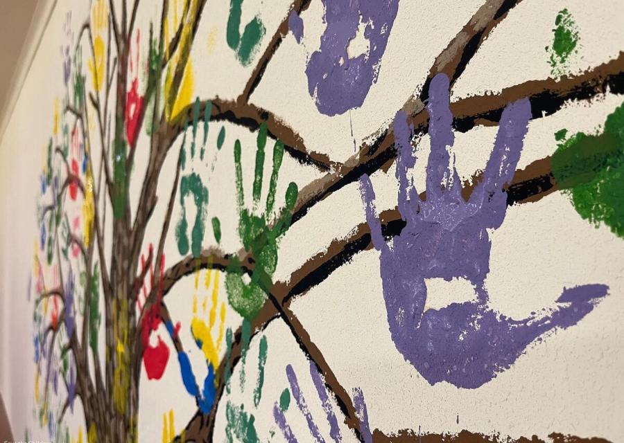 impronte mani colorate di bambini dipinte su muro attorno a rami 