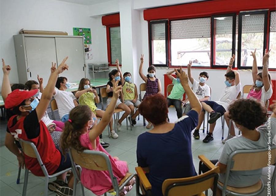 classe di bambini seduti in cerchio con le mani alzate 