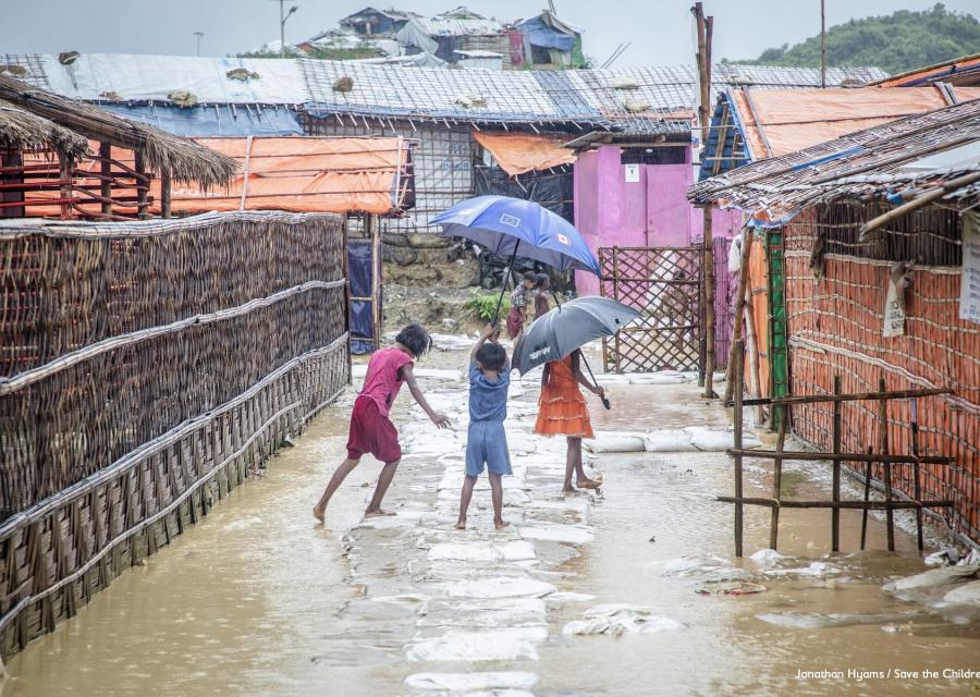 Tre bambini di spalle reggono ombrello e giocano in uno slum allagata del Bangladesh