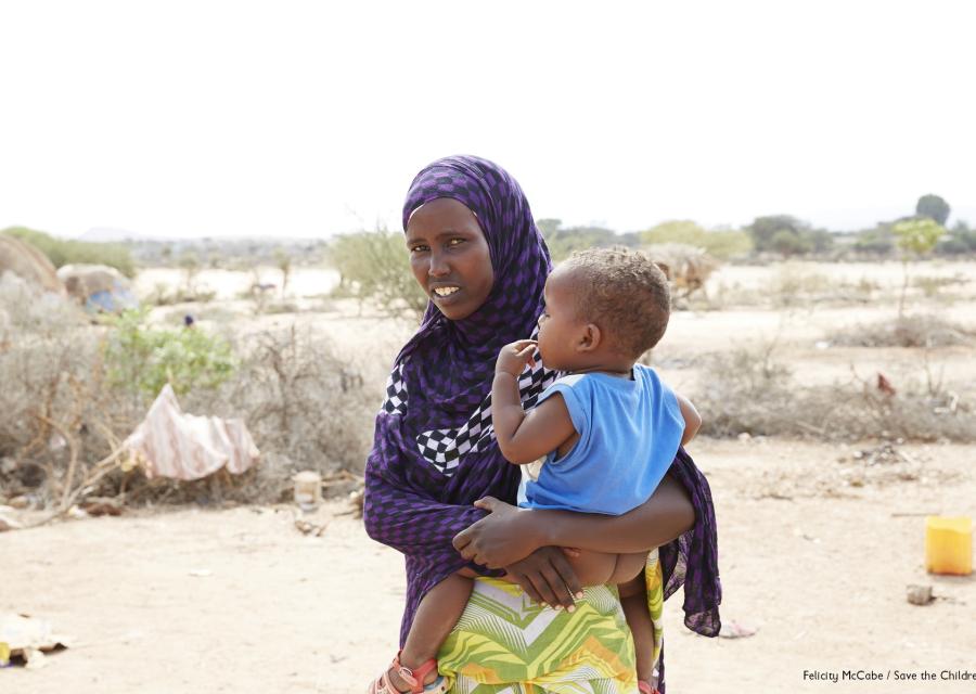 foto mezzo busto mamma con velo con il suo bambino in braccio, all aperto in una area colpita da siccità