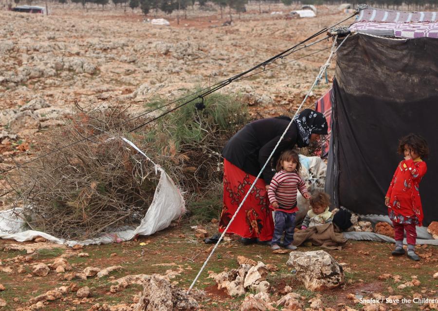 Tre bambini e una donna vicino alla tenda di un campo profughi.