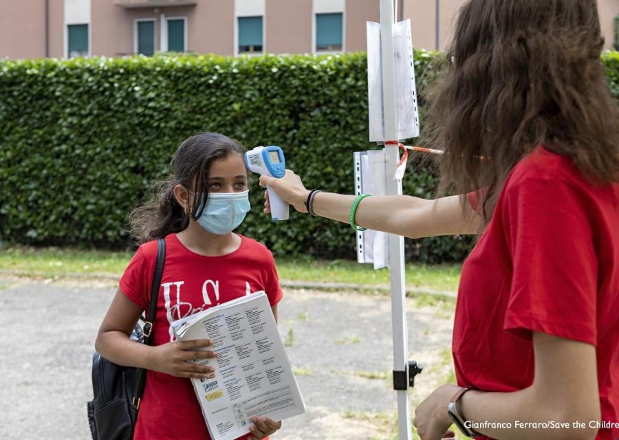 una operatrice misura la febbre con il termo scanner a una bambina con la mascherina chirurgica