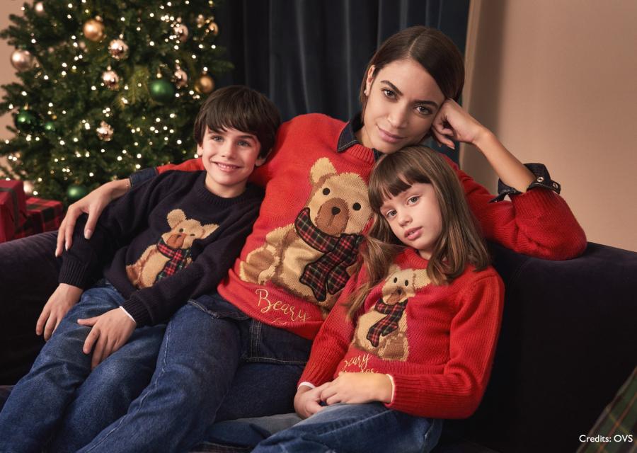 la cantante Elodie seduta su un divano insieme a una bambina e un bambino. Tutti e 3 indossano un maglione natalizio e alle loro spalle cè un albero di Natale