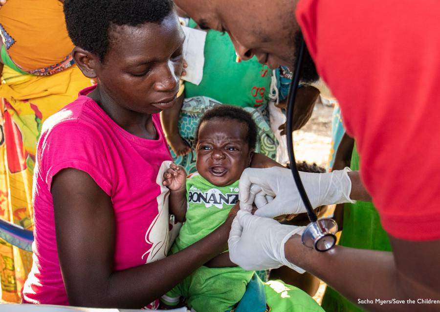 A sinistra operatore Save the Children visita un bambino tenuto in braccio dalla mamma. Siamo in Mozambico.