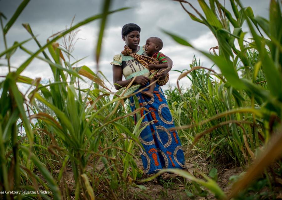 donna africana con bambino in braccio che piange contornati da un campo di pannocchie e sullo sfondo un cielo grigio 
